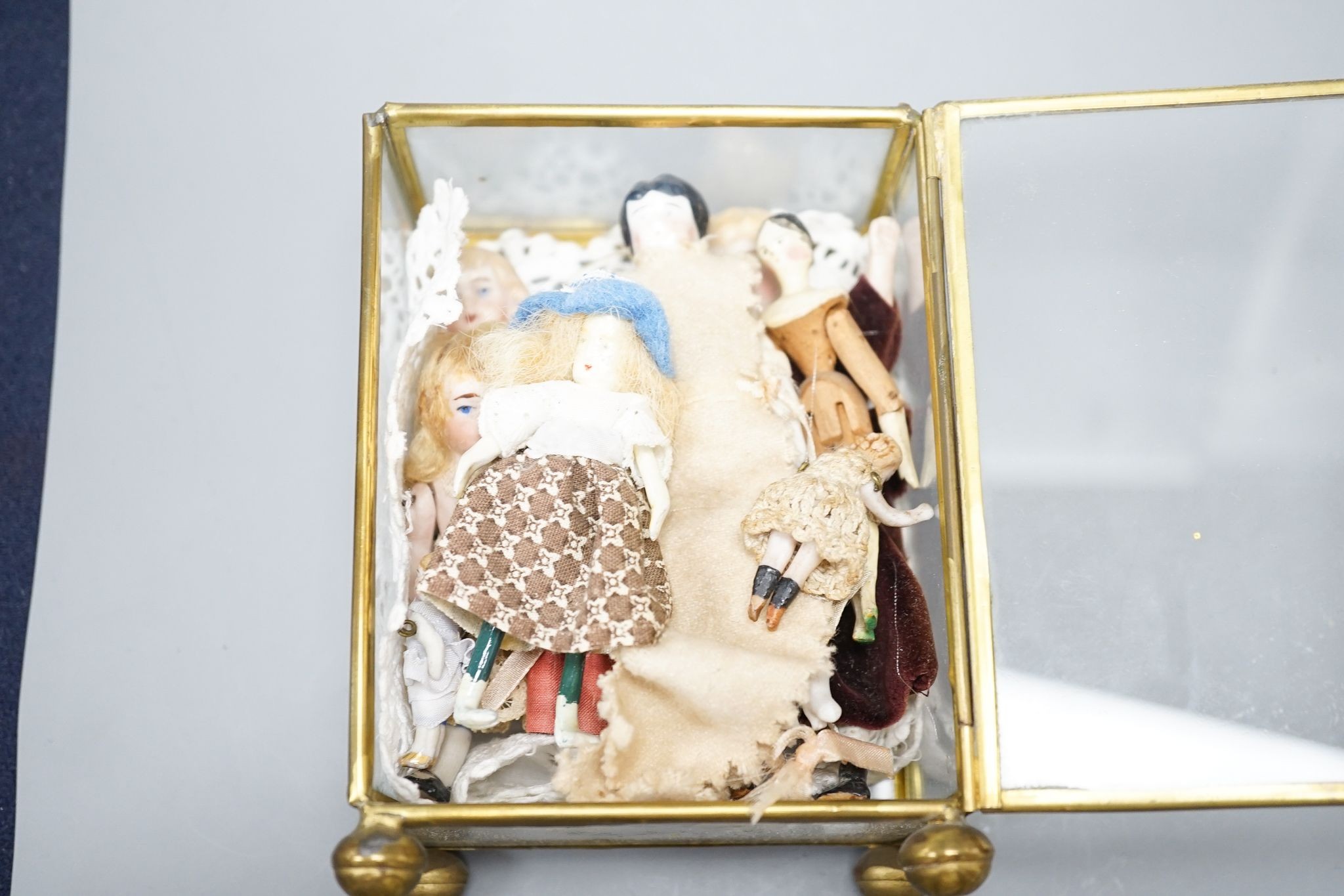 A collection of miniature bisque dolls and another larger doll in a wooden cradle, 11 dolls in total., Cradle 23.5 cms long.